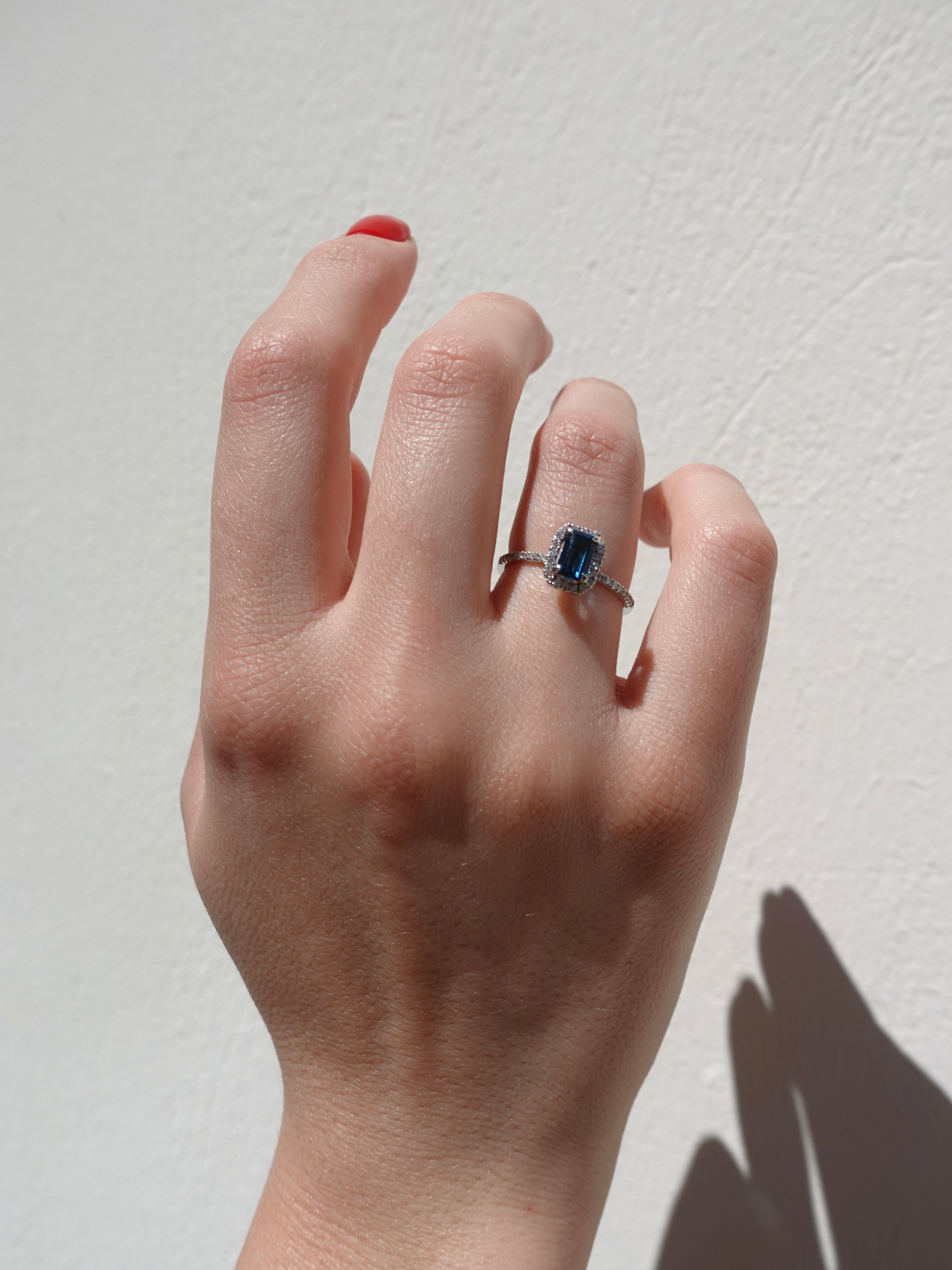 Hand wearing a ring with a blue gemstone on a light background