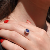Close-up of a hand wearing a ring with a blue sapphire gemstone.