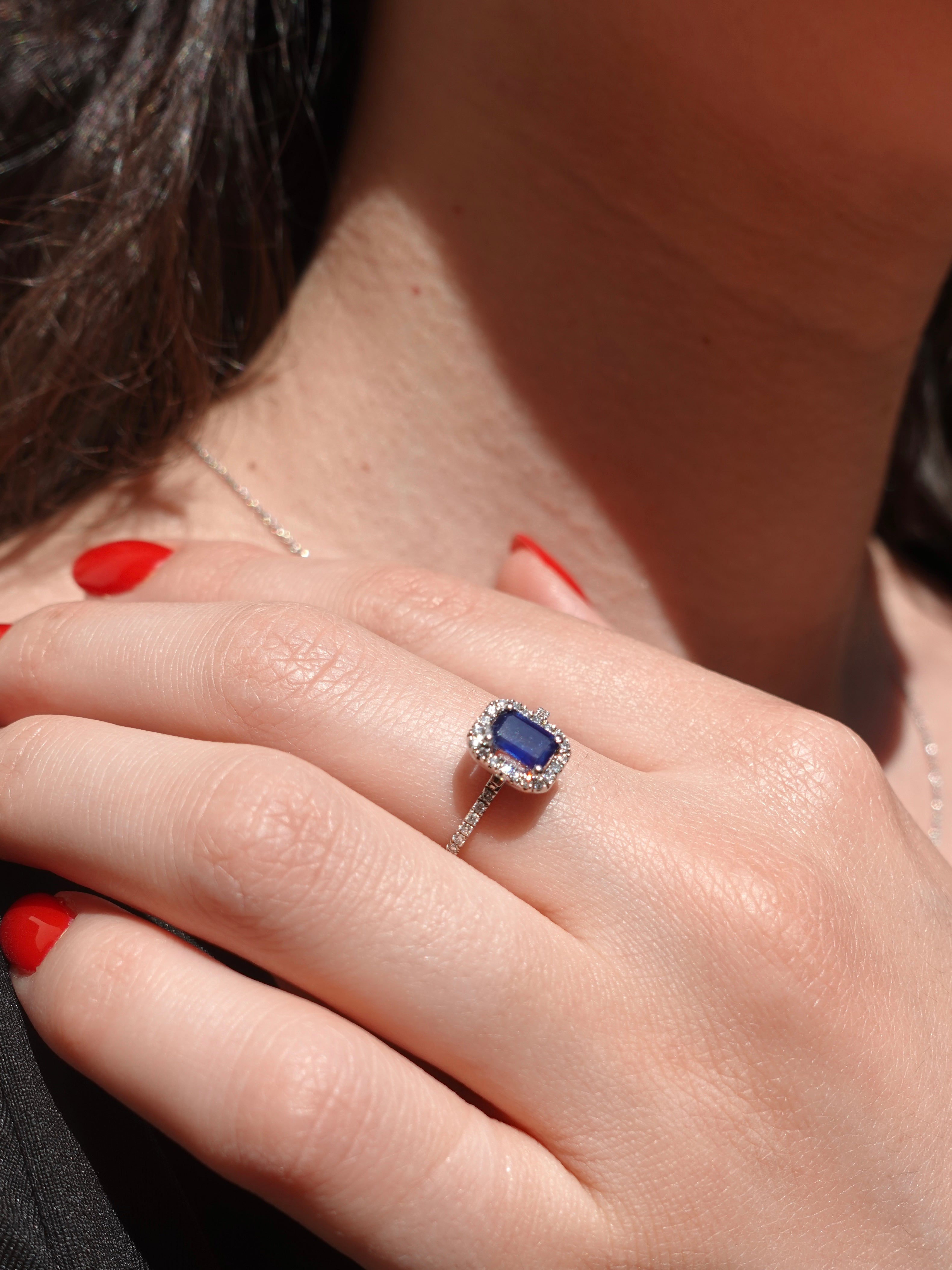 Close-up of a hand wearing a ring with a blue sapphire gemstone.