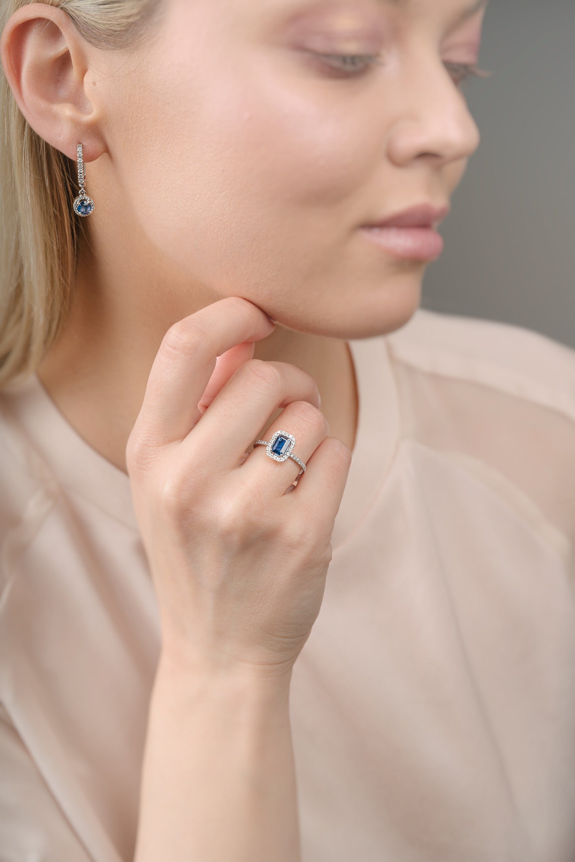 Close-up of a woman wearing a ring and an earring with blue sapphires, focusing on the jewelry.
