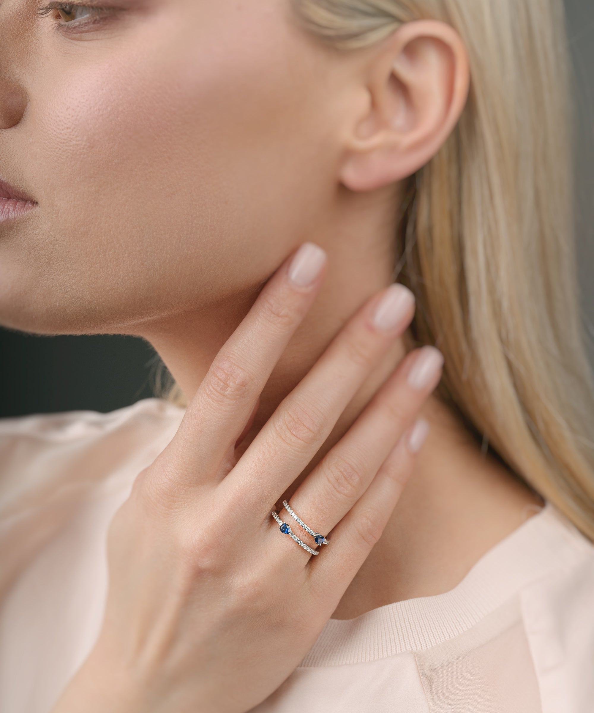 Woman wearing a ring with sapphires on her finger with a neutral background