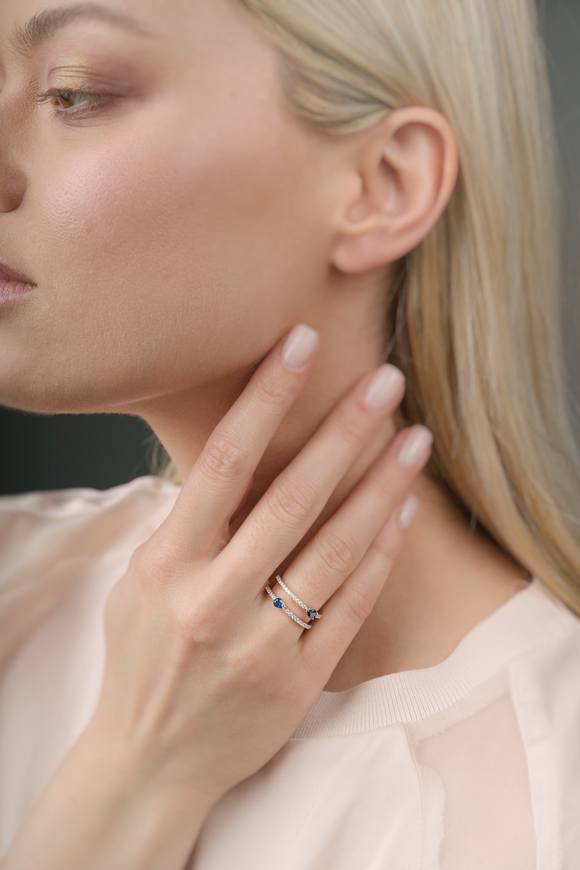 Woman wearing a ring with sapphires on her finger with a neutral background
