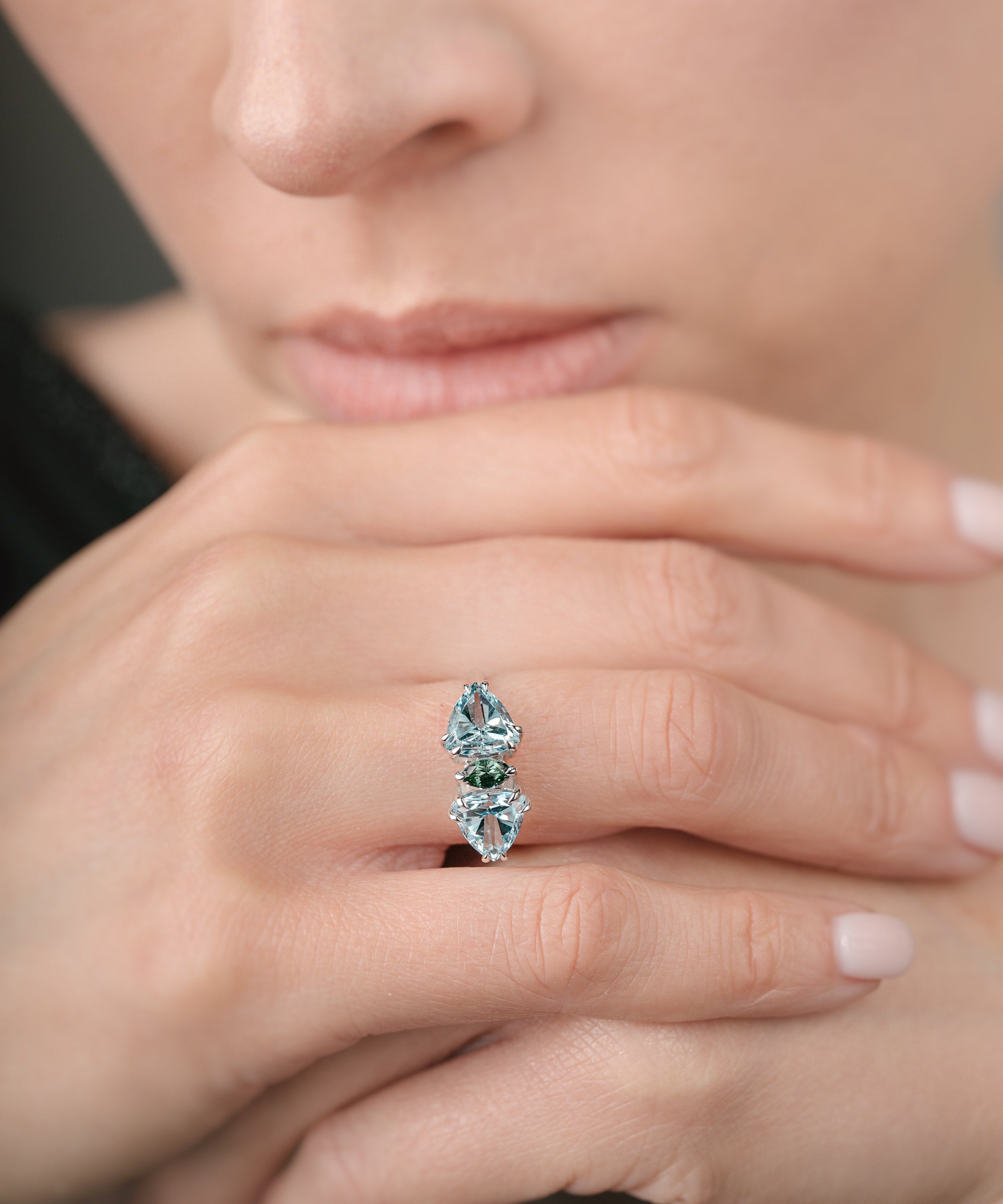 Close-up of a hand wearing a ring with green and blue gemstones.