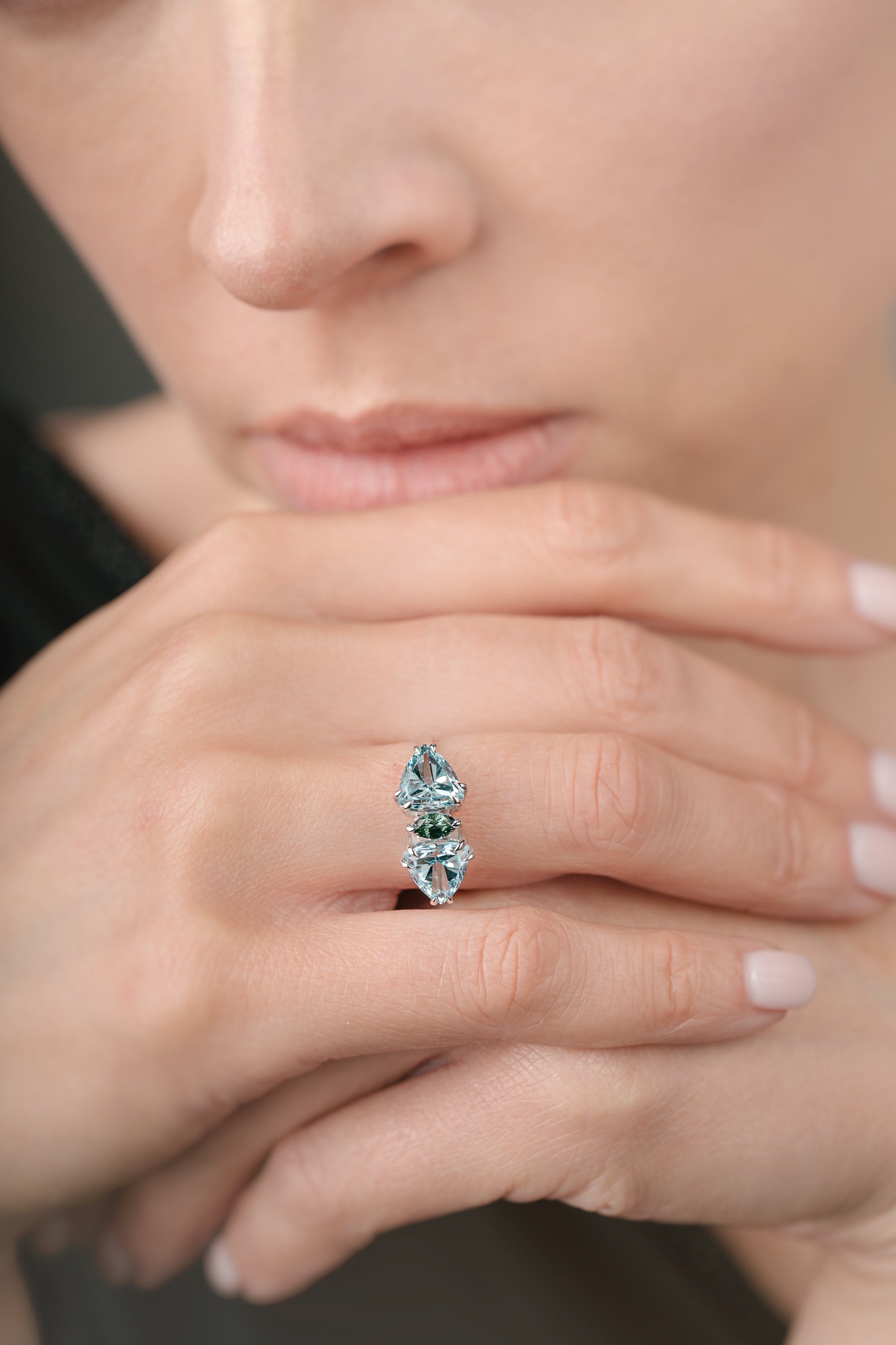 Close-up of a hand wearing a ring with green and blue gemstones.