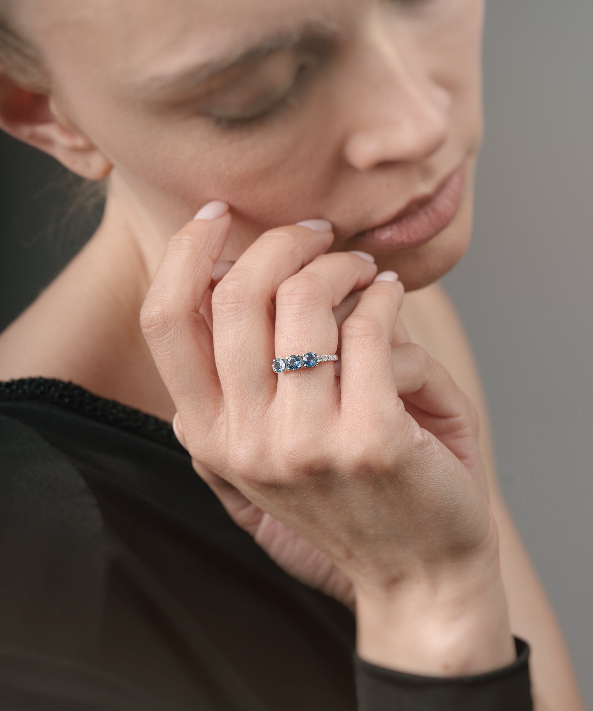 Close-up of a woman wearing a ring with three sapphires on a neutral background