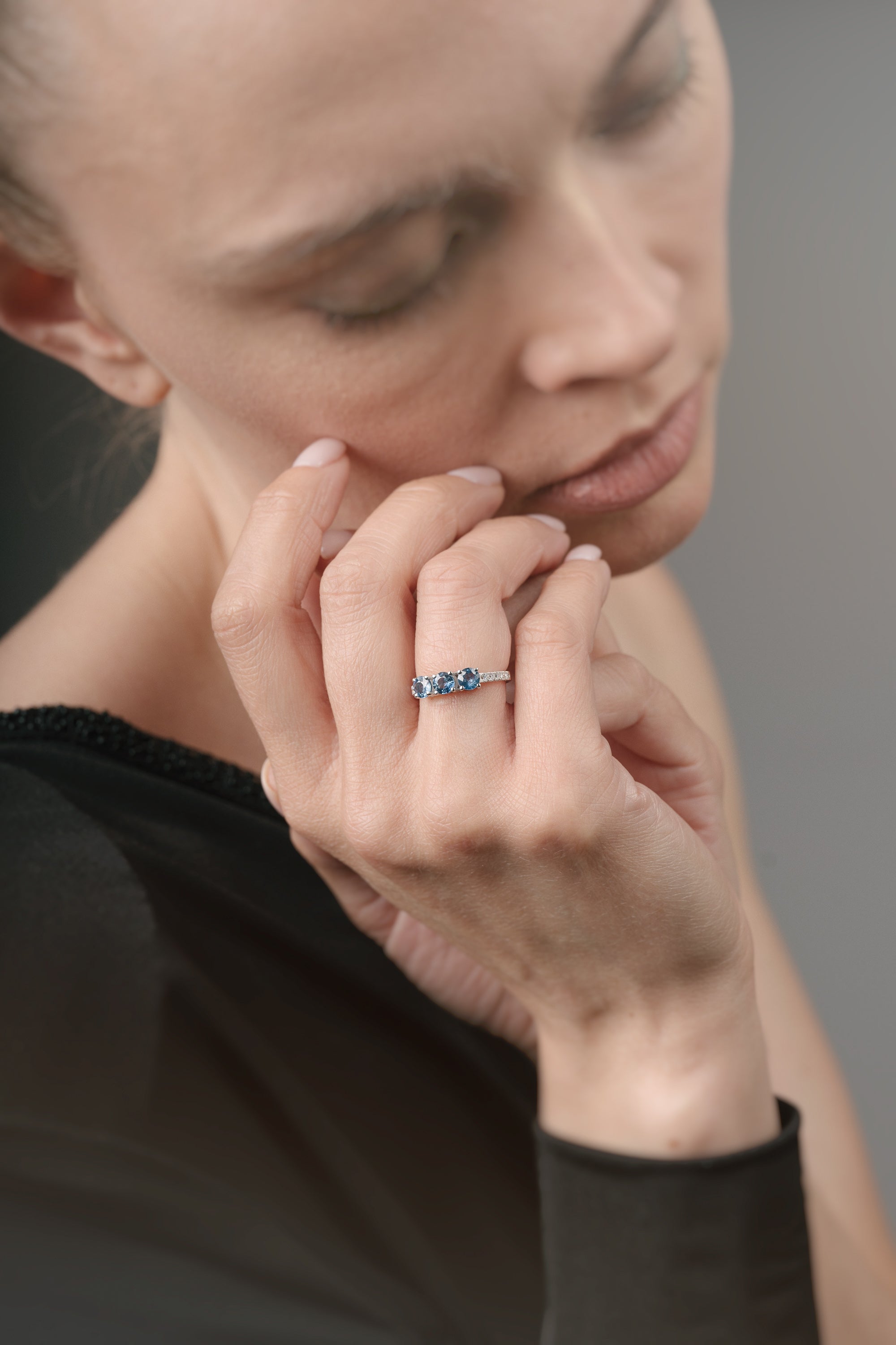 Close-up of a woman wearing a ring with three sapphires on a neutral background