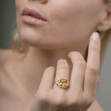 Close-up of a woman's hand wearing a gold ring with a yellow beryl central gemstone.