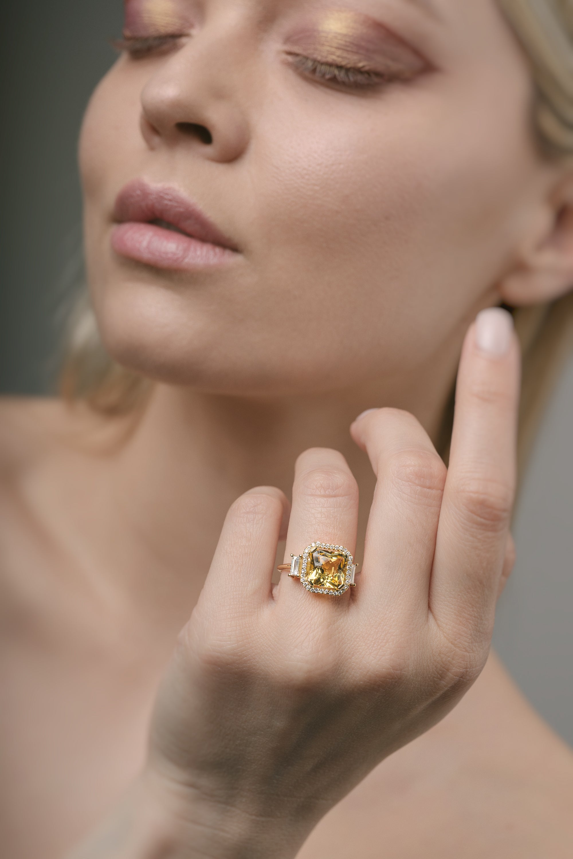 Close-up of a woman's hand wearing a gold ring with a yellow beryl central gemstone.