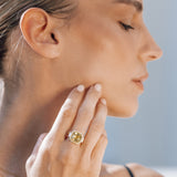 Woman wearing a gold ring with yellow gemstone on her finger, with a blurred background