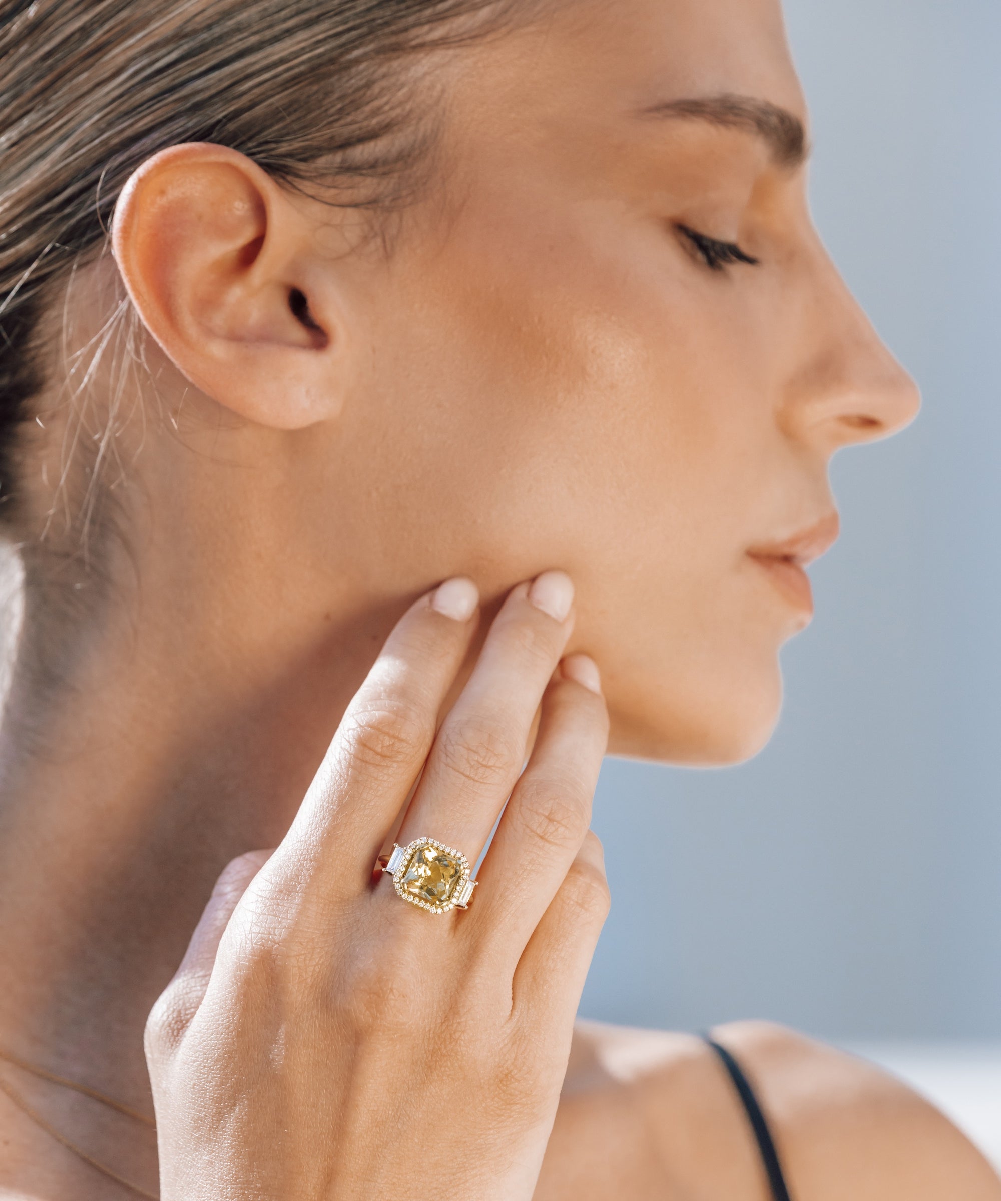 Woman wearing a gold ring with yellow gemstone on her finger, with a blurred background