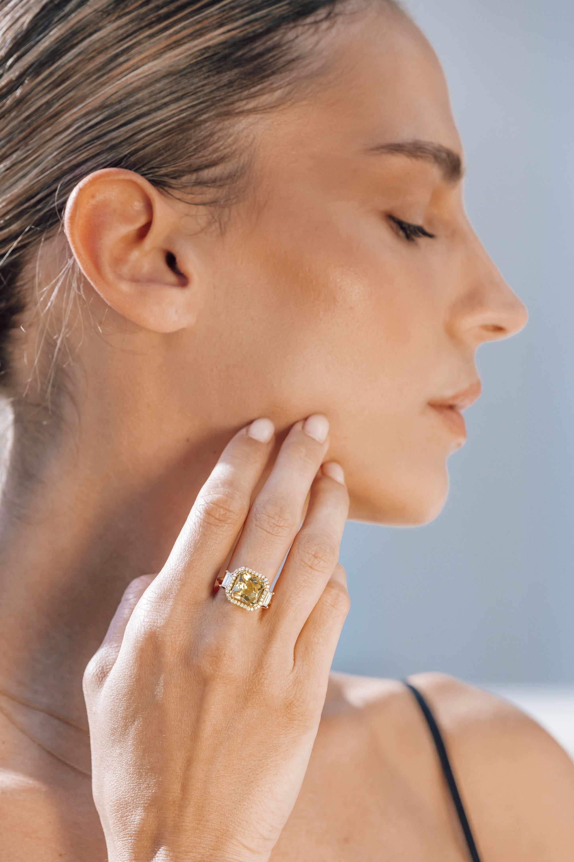 Woman wearing a gold ring with yellow gemstone on her finger, with a blurred background