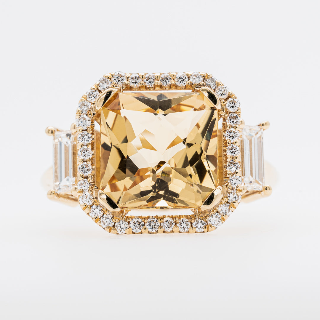 Gold ring with a large yellow beryl gemstone and smaller diamonds on a light gray background