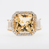Gold ring with a large yellow beryl gemstone and smaller diamonds on a light gray background