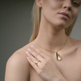 Woman wearing a gold teardrop necklace and sunburst ring on a neutral background