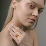 Woman wearing a gold sunburst ring on her hand against a neutral background