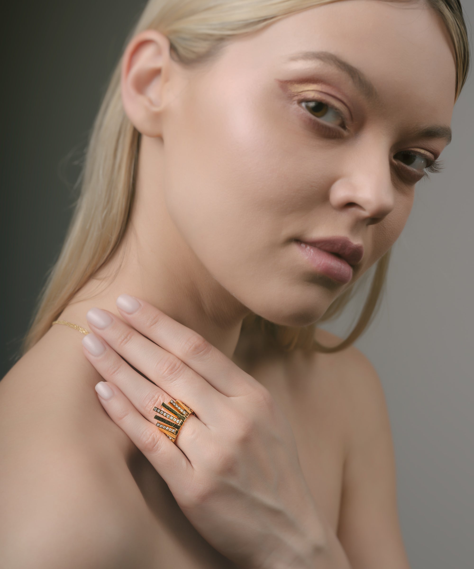Woman wearing a gold sunburst ring on her hand against a neutral background