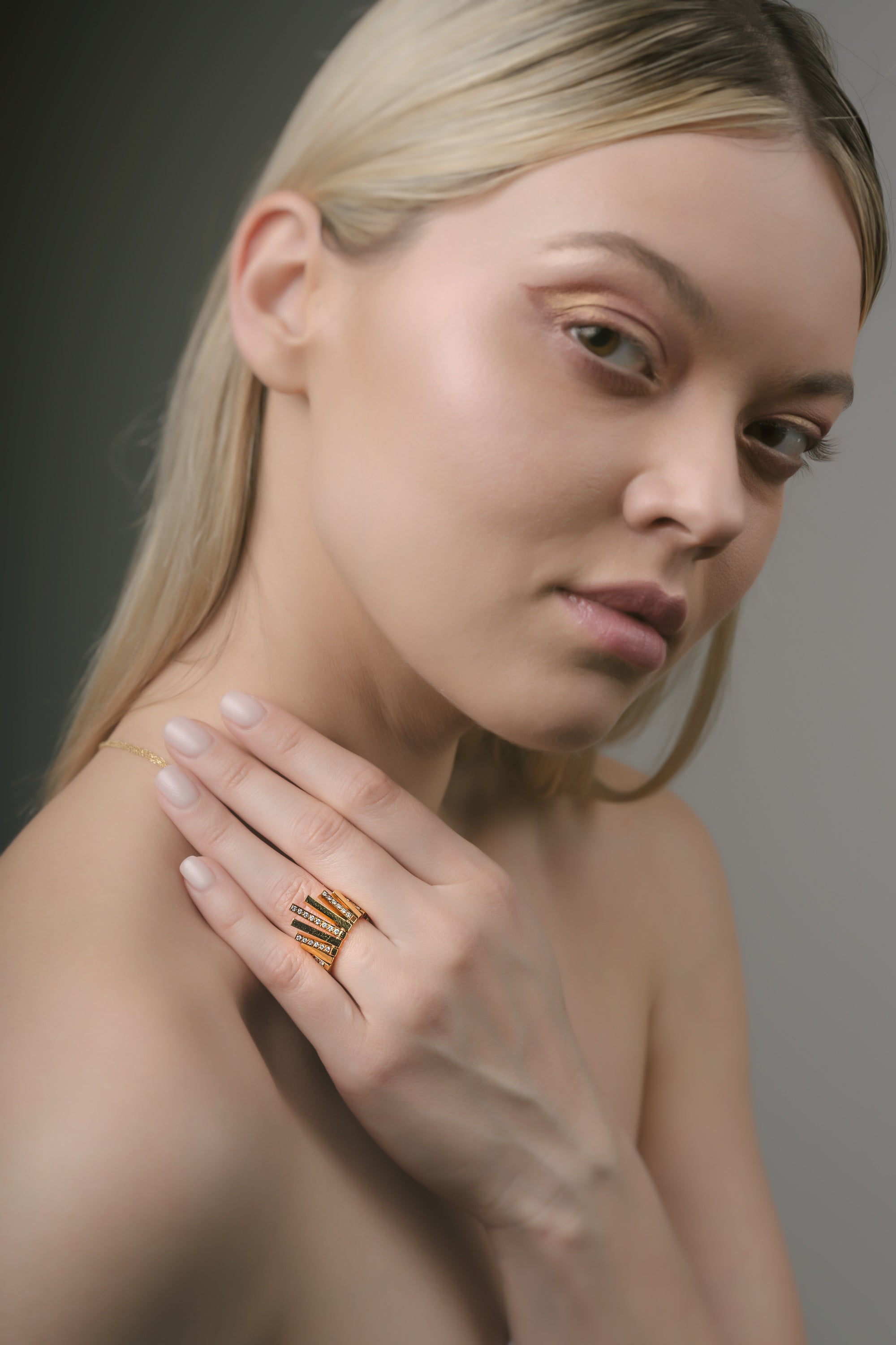 Woman wearing a gold sunburst ring on her hand against a neutral background
