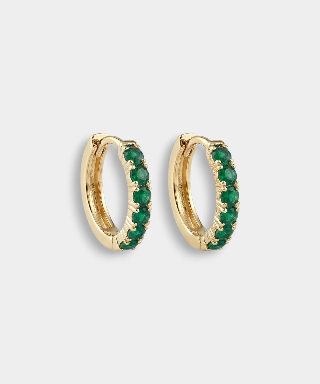 Gold hoop earrings with emeralds on a light gray background