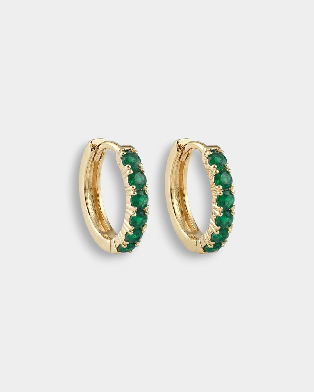 Gold hoop earrings with emeralds on a light gray background