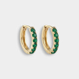 Gold hoop earrings with emeralds on a light gray background