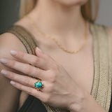 Woman wearing a gold ring with a green gemstone on her finger.