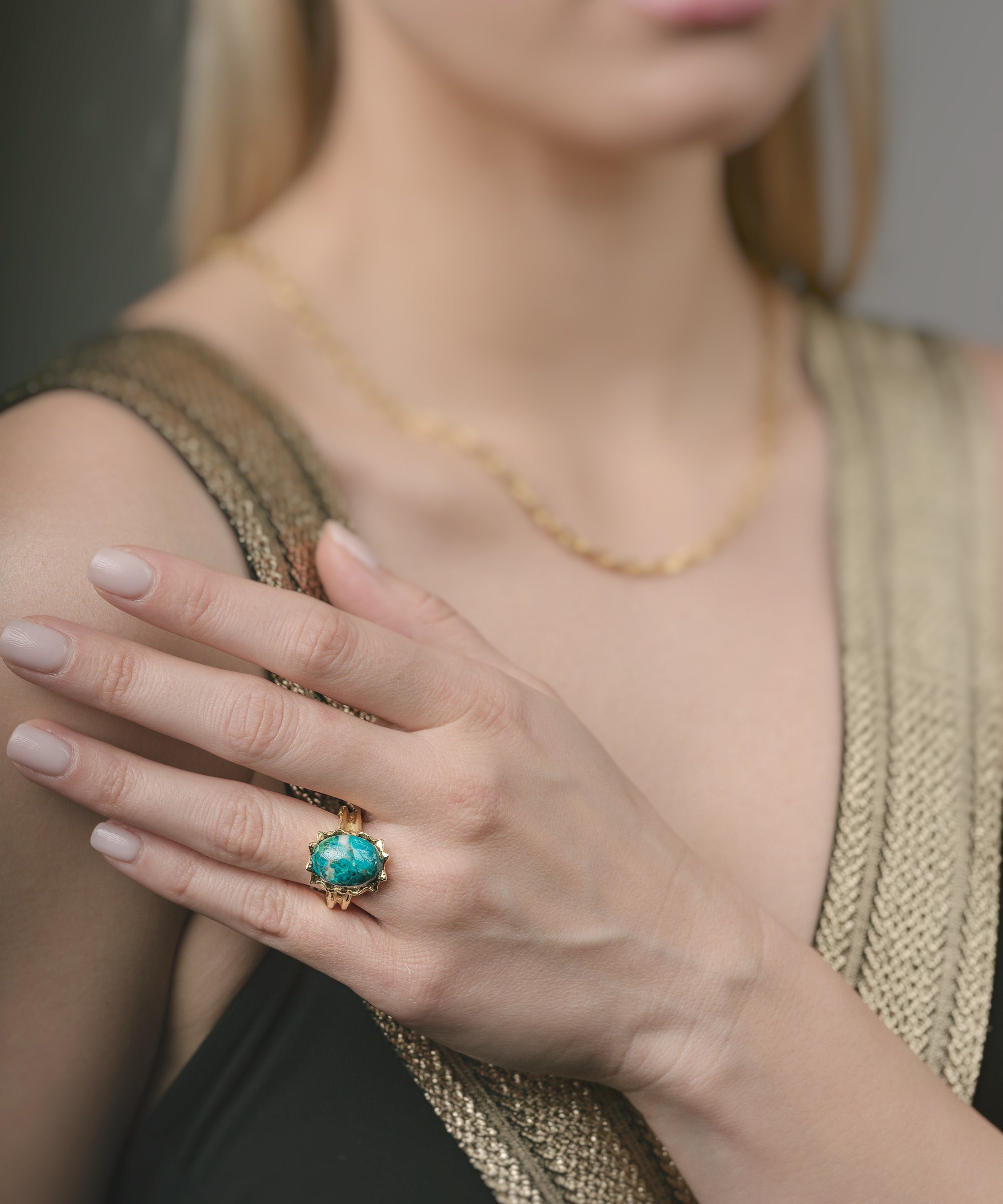 Woman wearing a gold ring with a green gemstone on her finger.