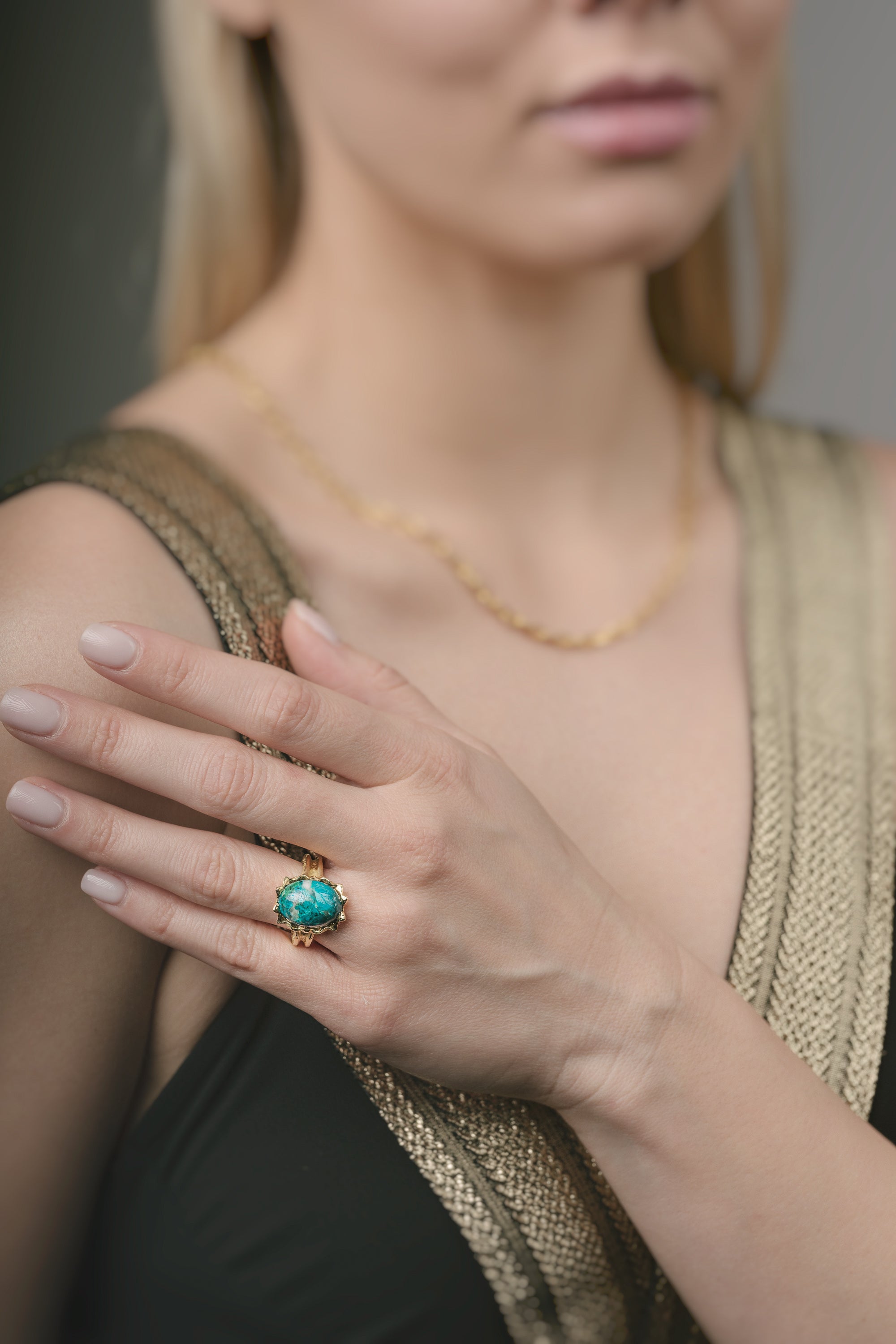 Woman wearing a gold ring with a green gemstone on her finger.
