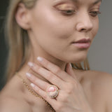 Woman wearing a gold ring with a pink gemstone against a neutral background