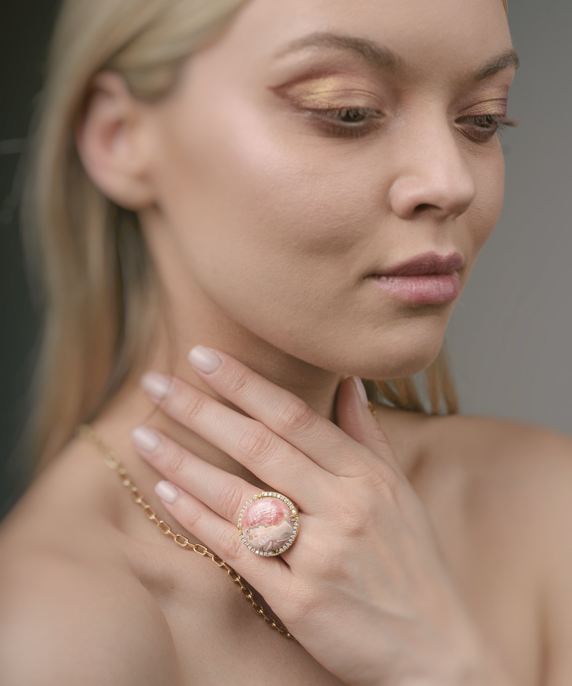 Woman wearing a gold ring with a pink gemstone against a neutral background
