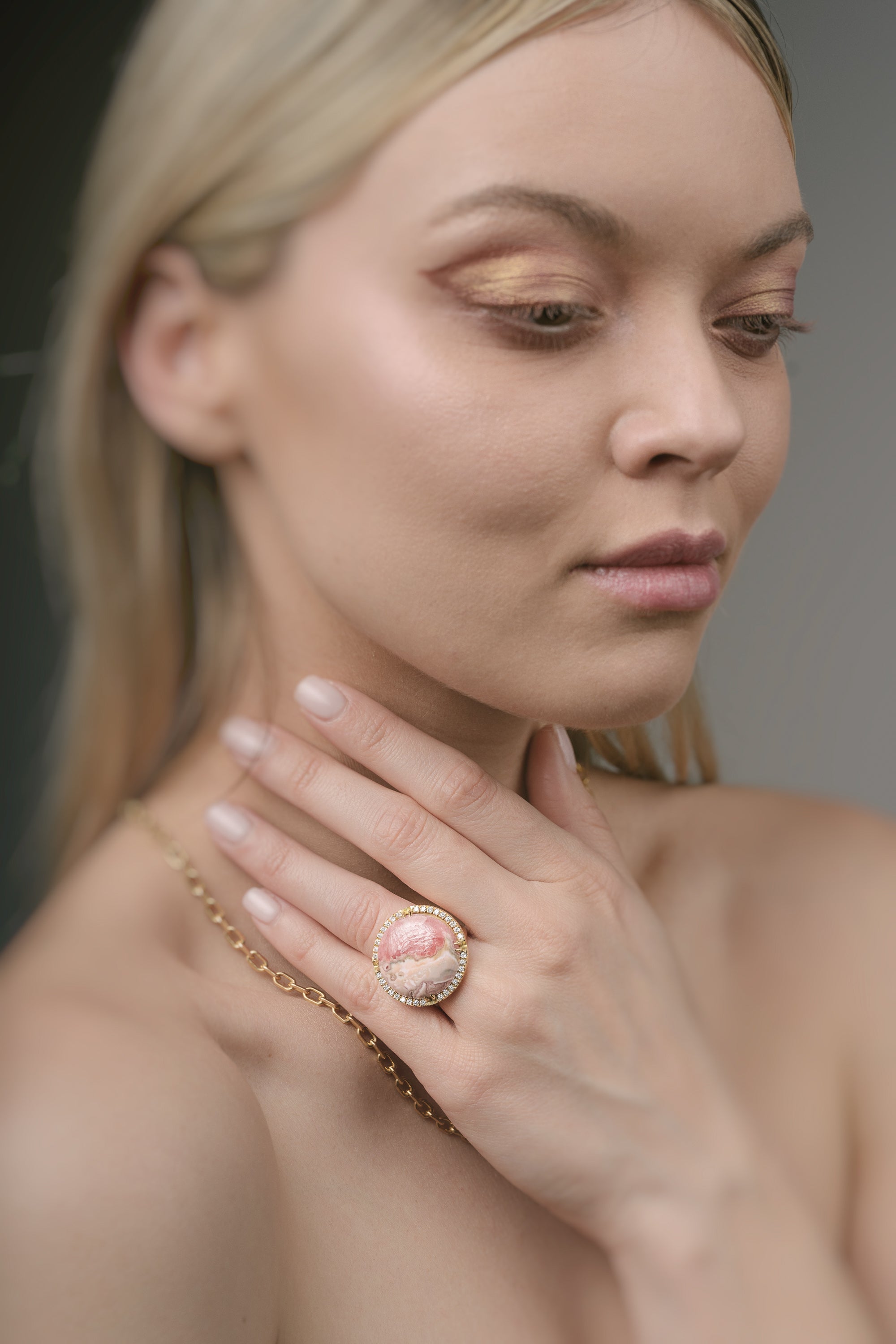 Woman wearing a gold ring with a pink gemstone against a neutral background