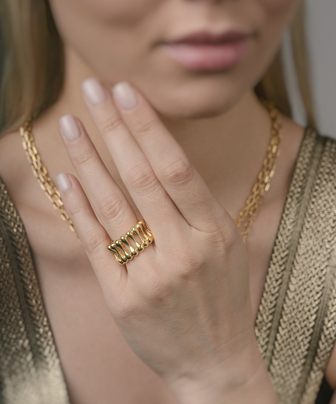 Close-up of a person wearing gold jewelry including a ring and necklace.