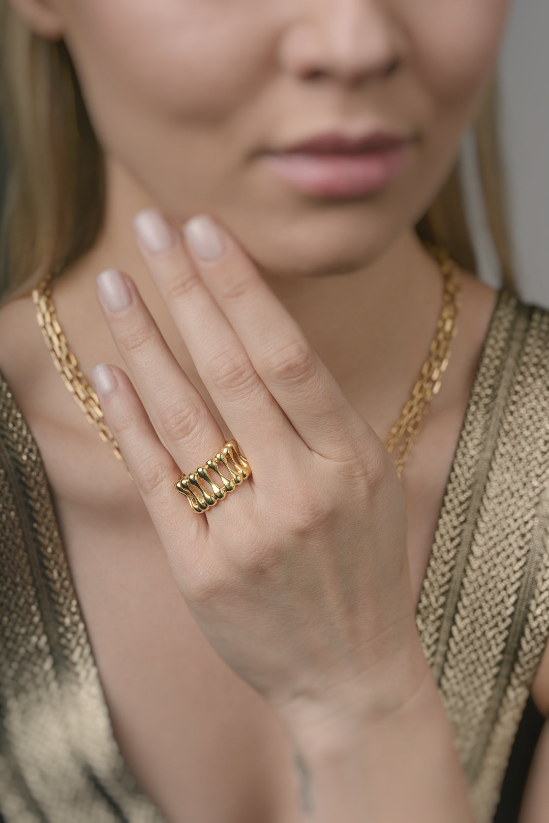 Close-up of a person wearing gold jewelry including a ring and necklace.