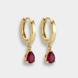 Gold hoop earrings with red teardrop rubies on a light gray background