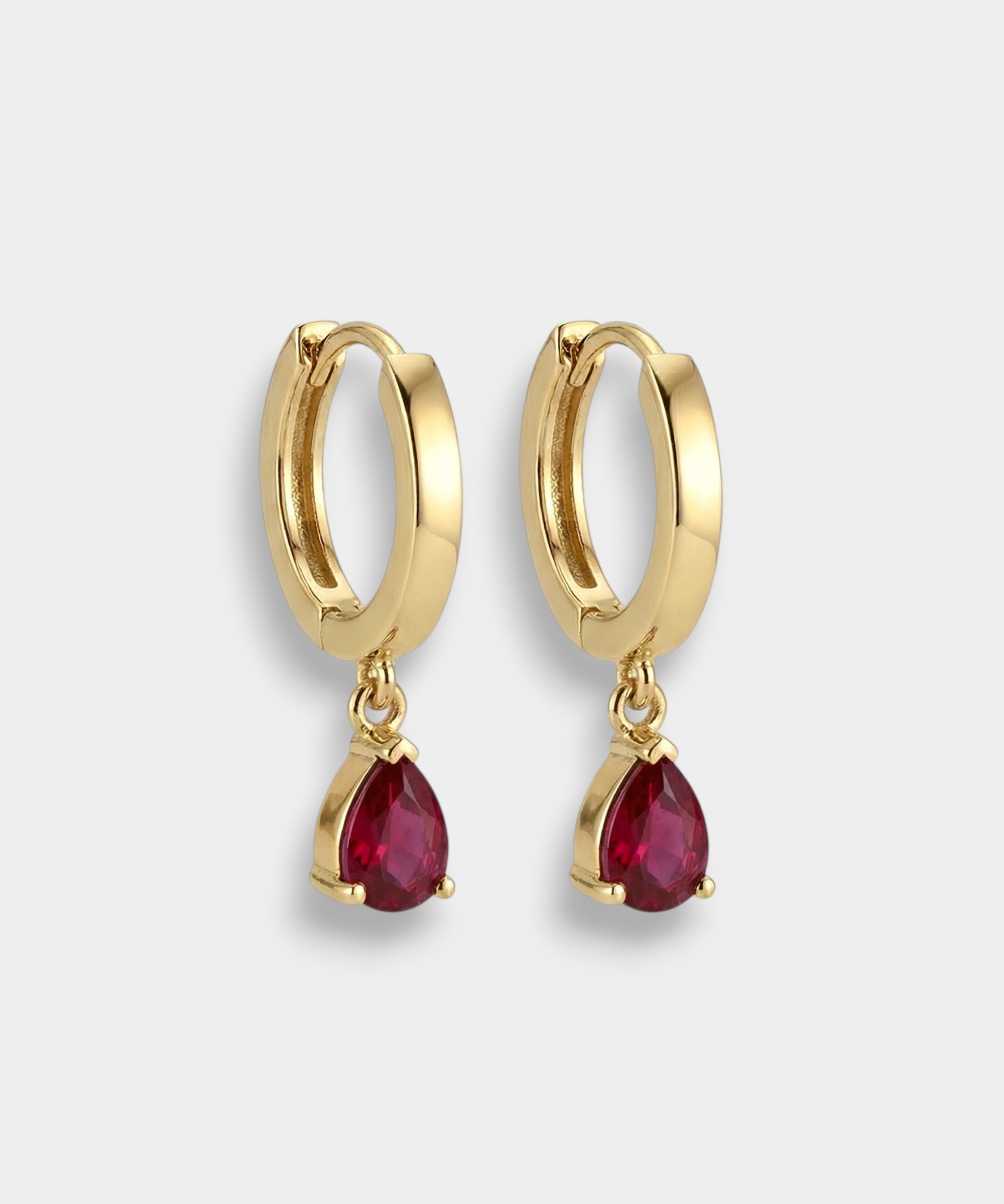 Gold hoop earrings with red teardrop rubies on a light gray background