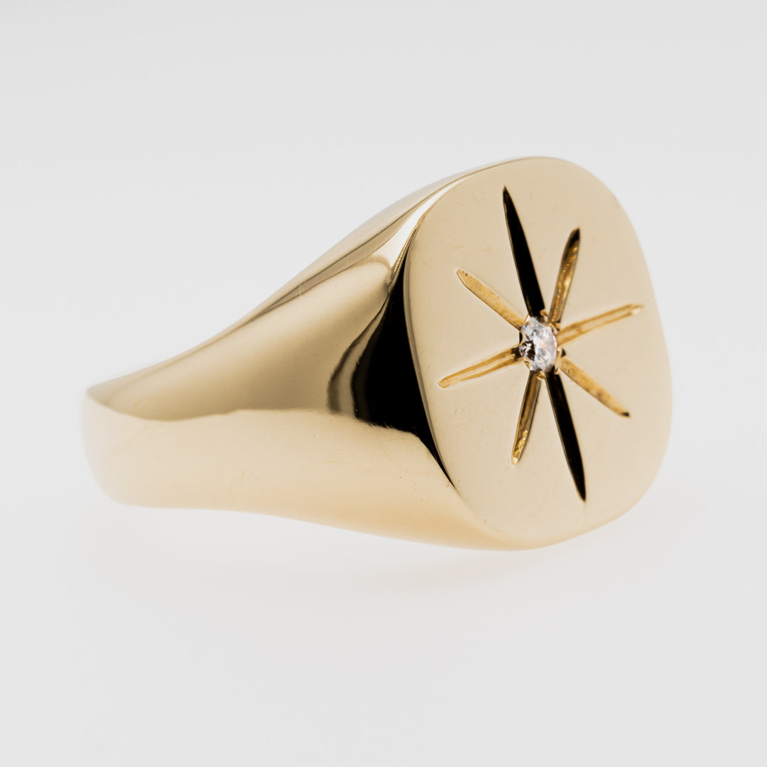 Gold ring with star design and diamond on a light gray background