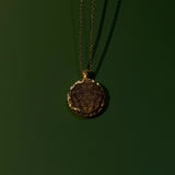 Gold necklace with a round pendant on a dark green background