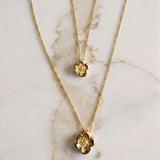 Two gold necklaces with floral pendants on a marble surface