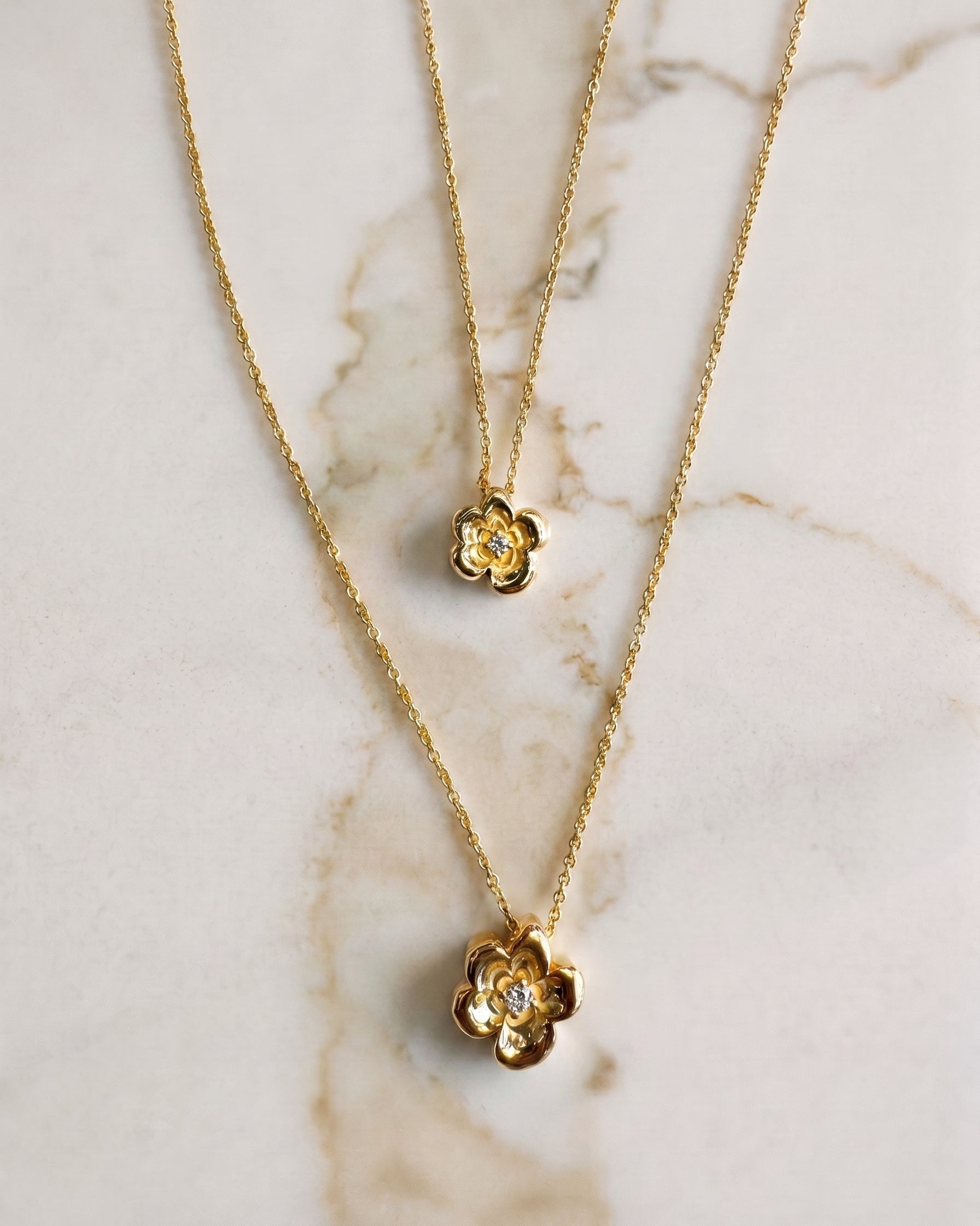 Two gold necklaces with floral pendants on a marble surface