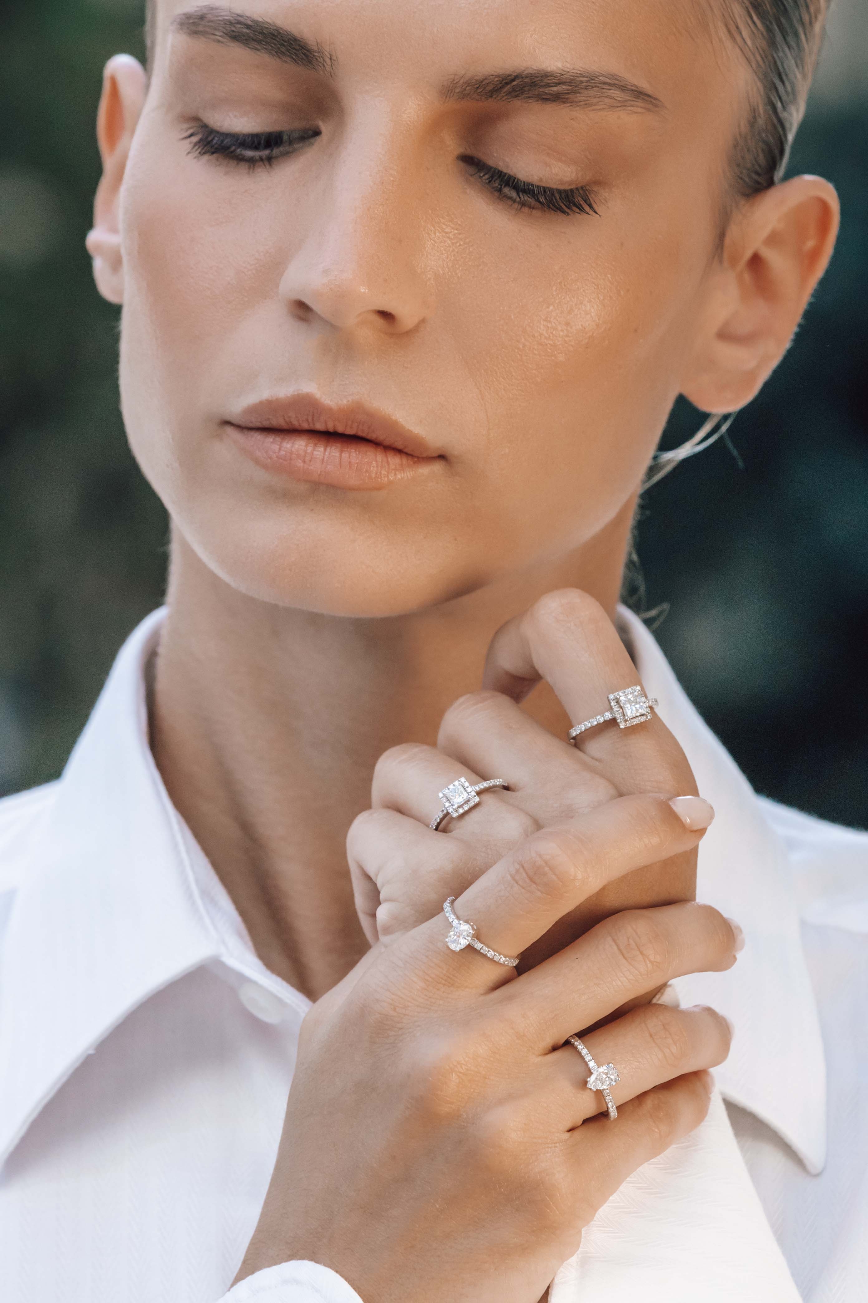 Close-up of a woman wearing multiple engagement diamond rings on her fingers.