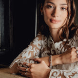 Woman wearing a lace top with multiple diamond rings, sitting indoors.
