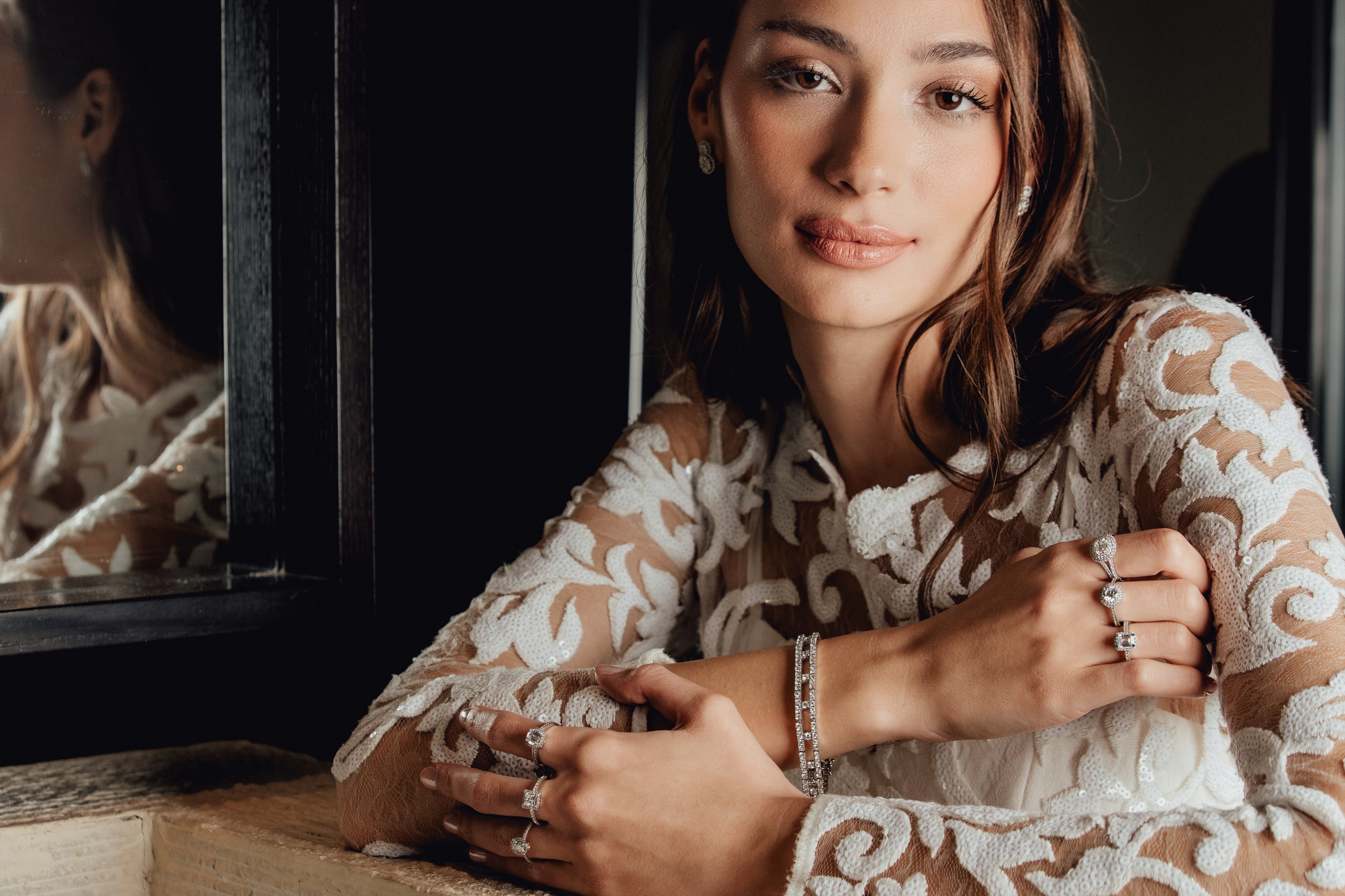 Woman wearing a lace top with multiple diamond rings, sitting indoors.