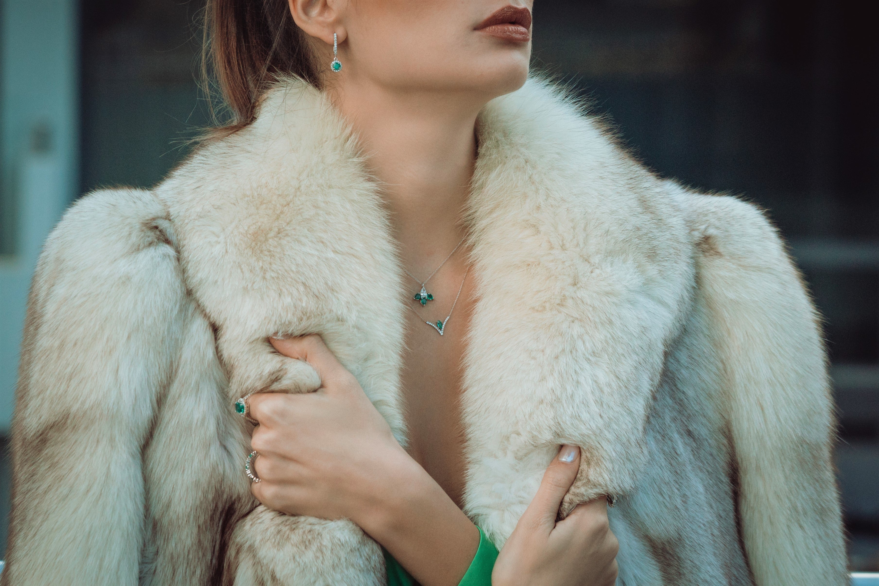 Close-up of a person wearing a fur coat and emerald jewellery with a blurred background