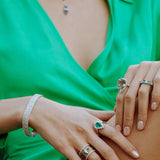 Close-up of a person wearing multiple rings and a bracelet on a green outfit.