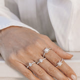 Hand wearing multiple engagement rings with diamond accents on a light background