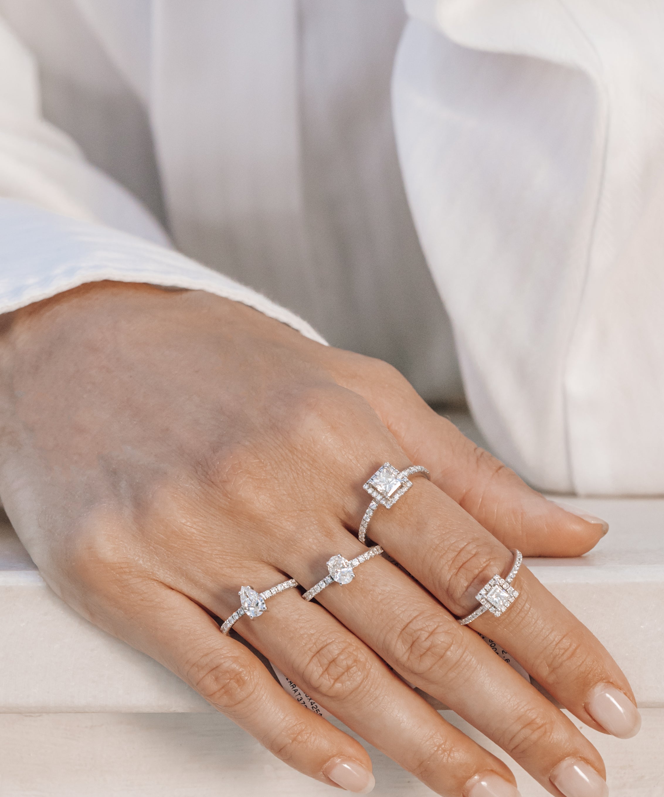 Hand wearing multiple engagement rings with diamond accents on a light background