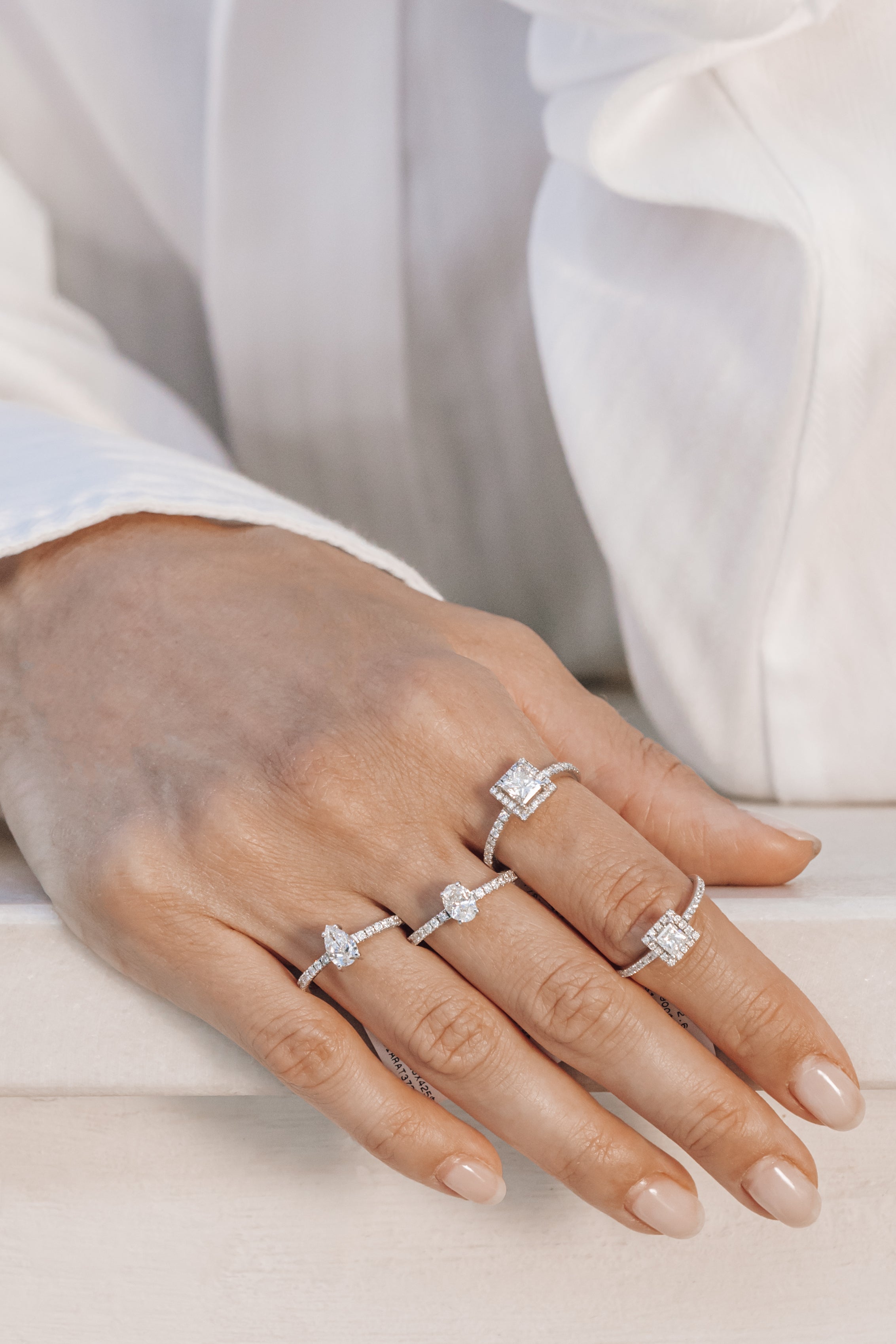 Hand wearing multiple engagement rings with diamond accents on a light background