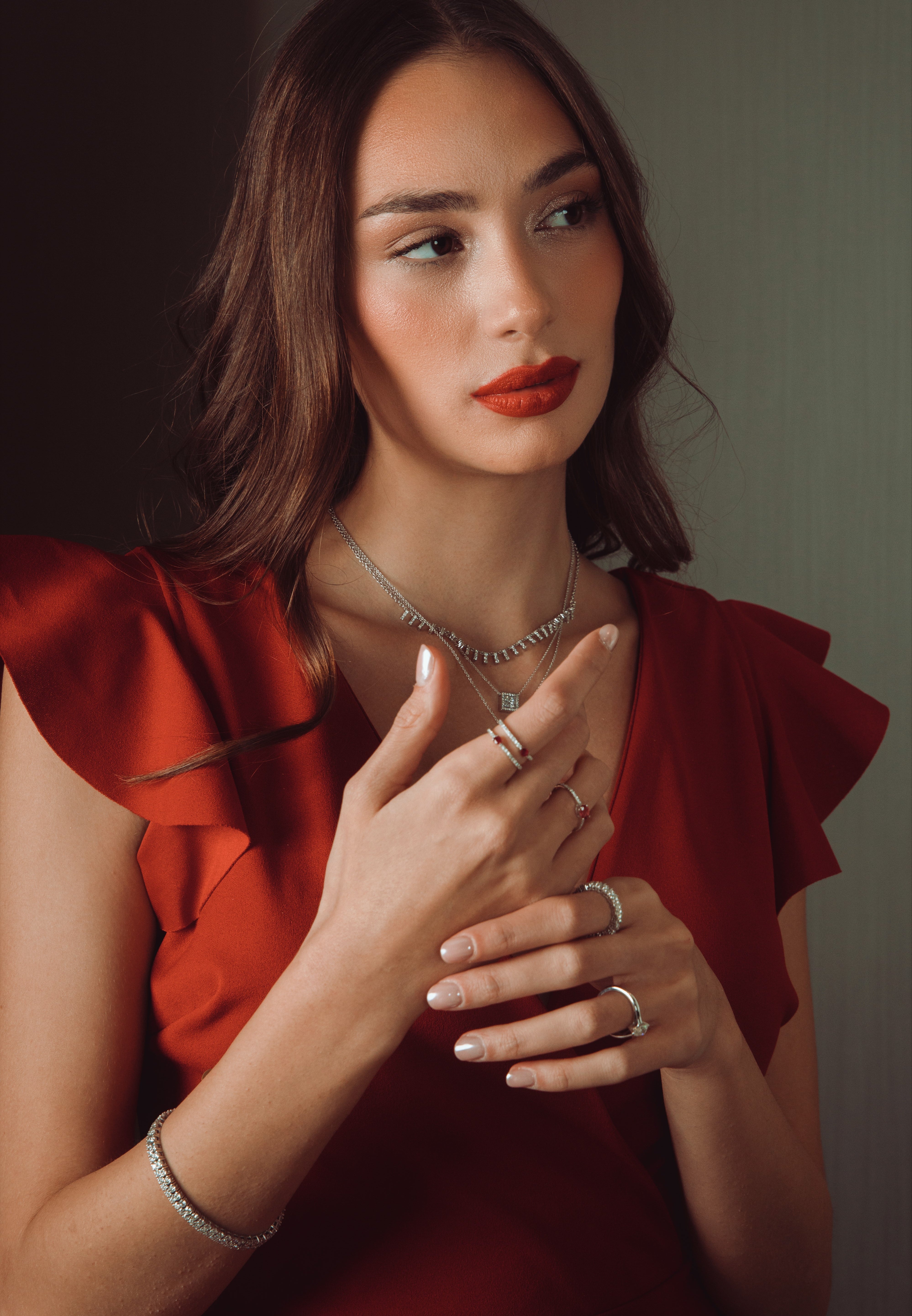 Woman wearing a red dress with jewelry against a neutral background