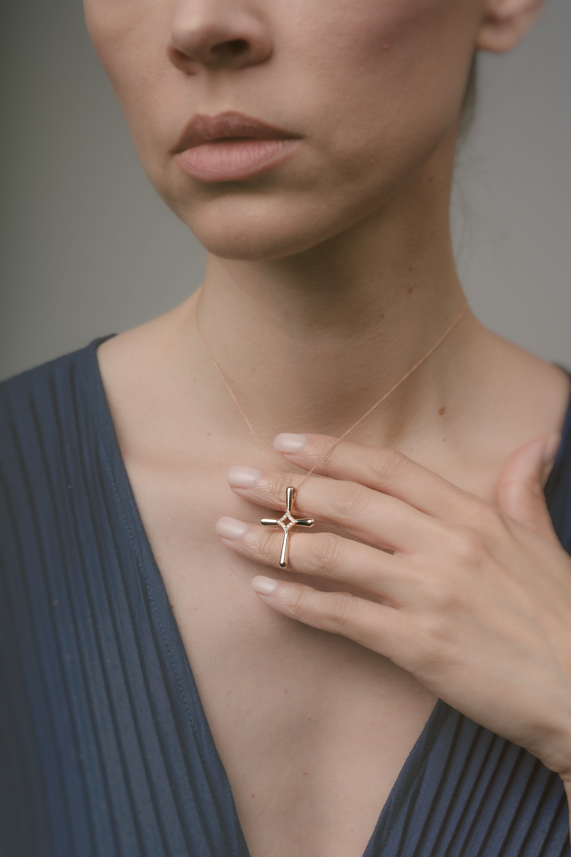 Woman wearing a gold necklace with a cross pendant, holding it close to her chest.