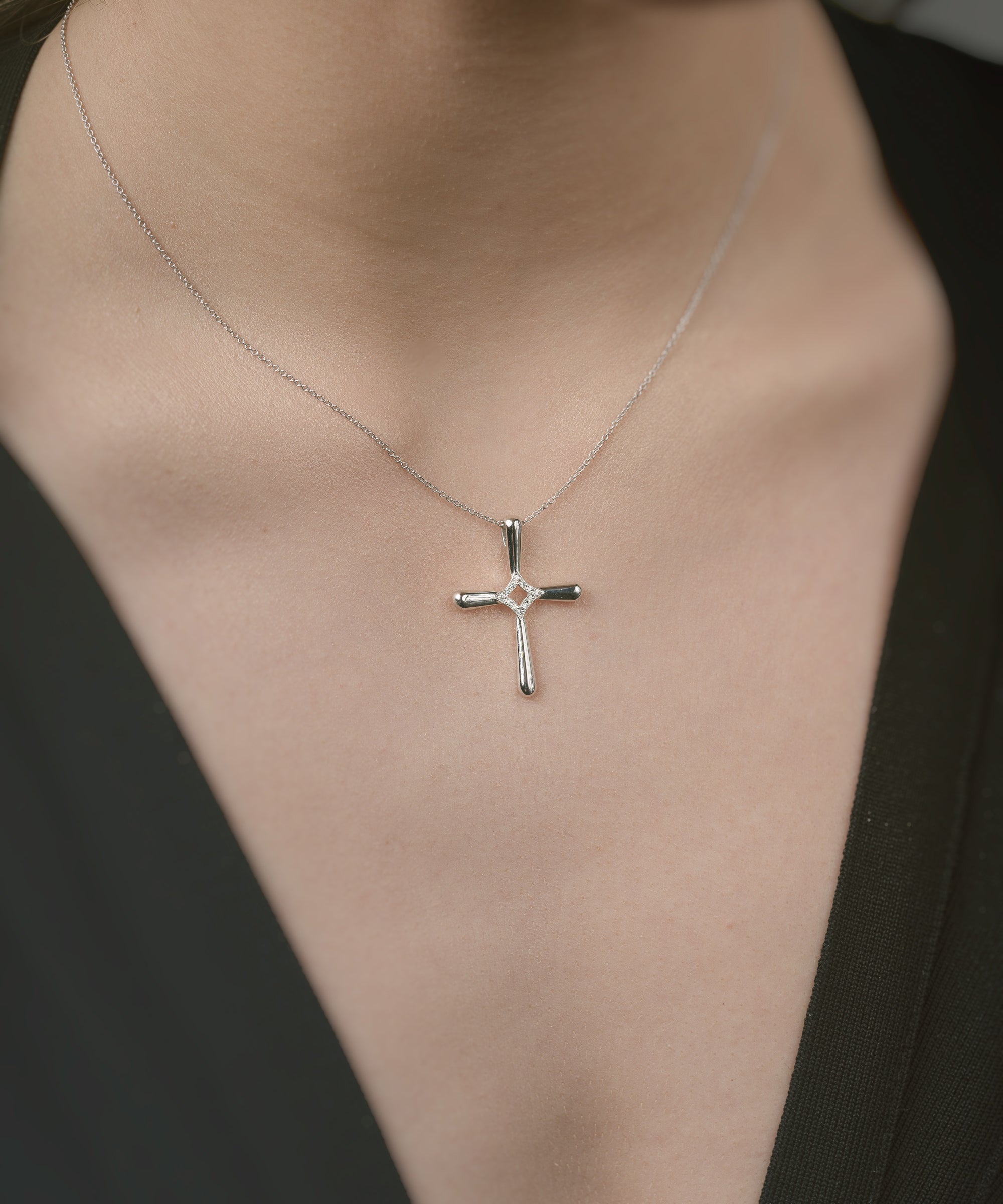 White gold cross necklace on a person wearing a black top