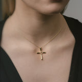 Gold cross necklace on a person wearing a black top against a neutral background